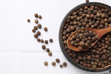 Photo of Dry allspice berries (Jamaica pepper) on white tiled table, top view. Space for text