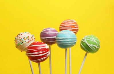 Many bright delicious cake pops on color background