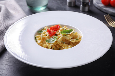 Photo of Delicious pasta with tomatoes and basil served on black table, closeup