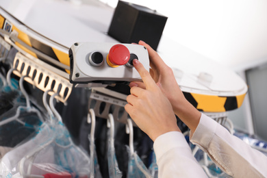 Worker pressing button on control panel of garment conveyor at modern dry-cleaner's, closeup