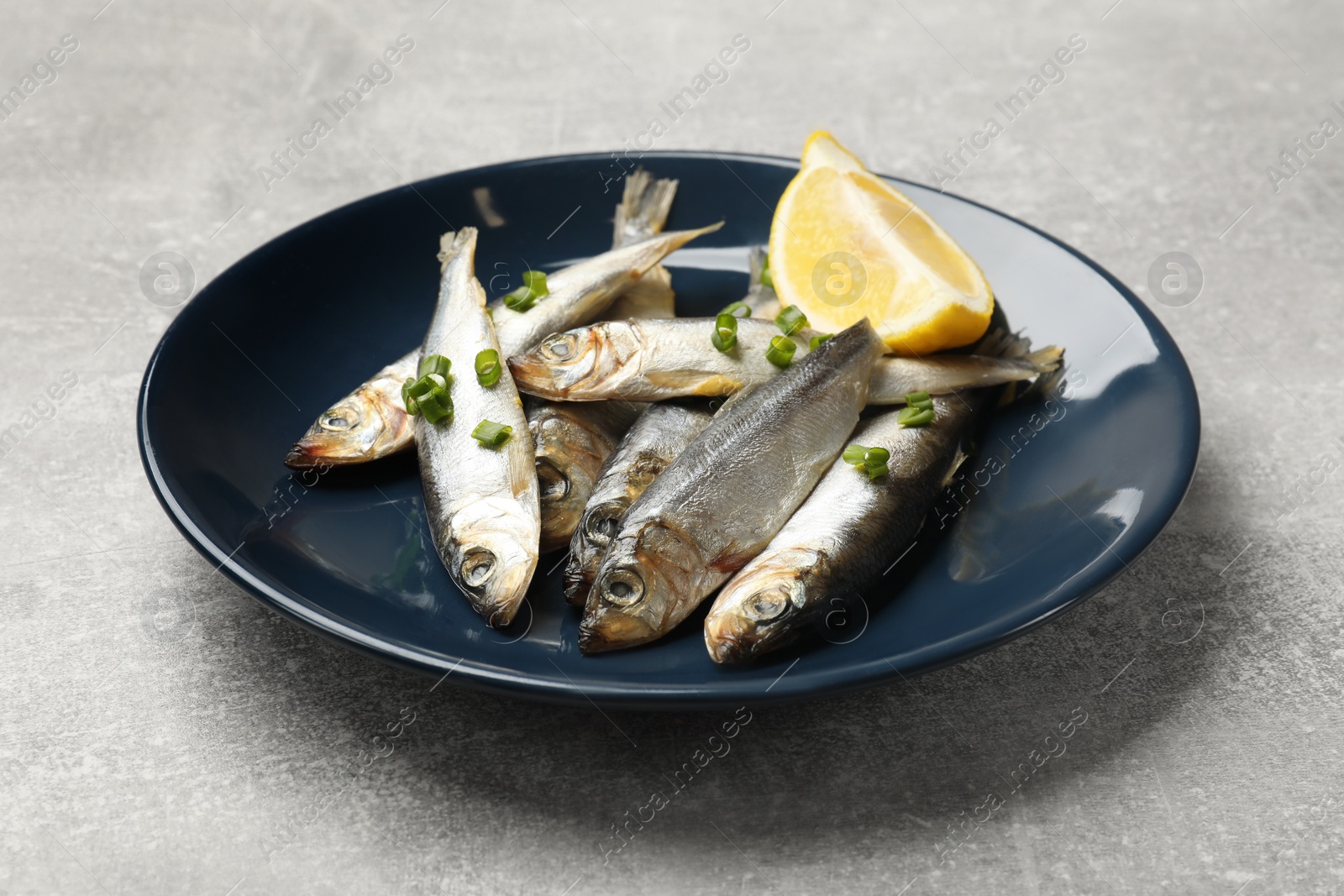 Photo of Fresh raw sprats, green onion and cut lemon on grey table, closeup