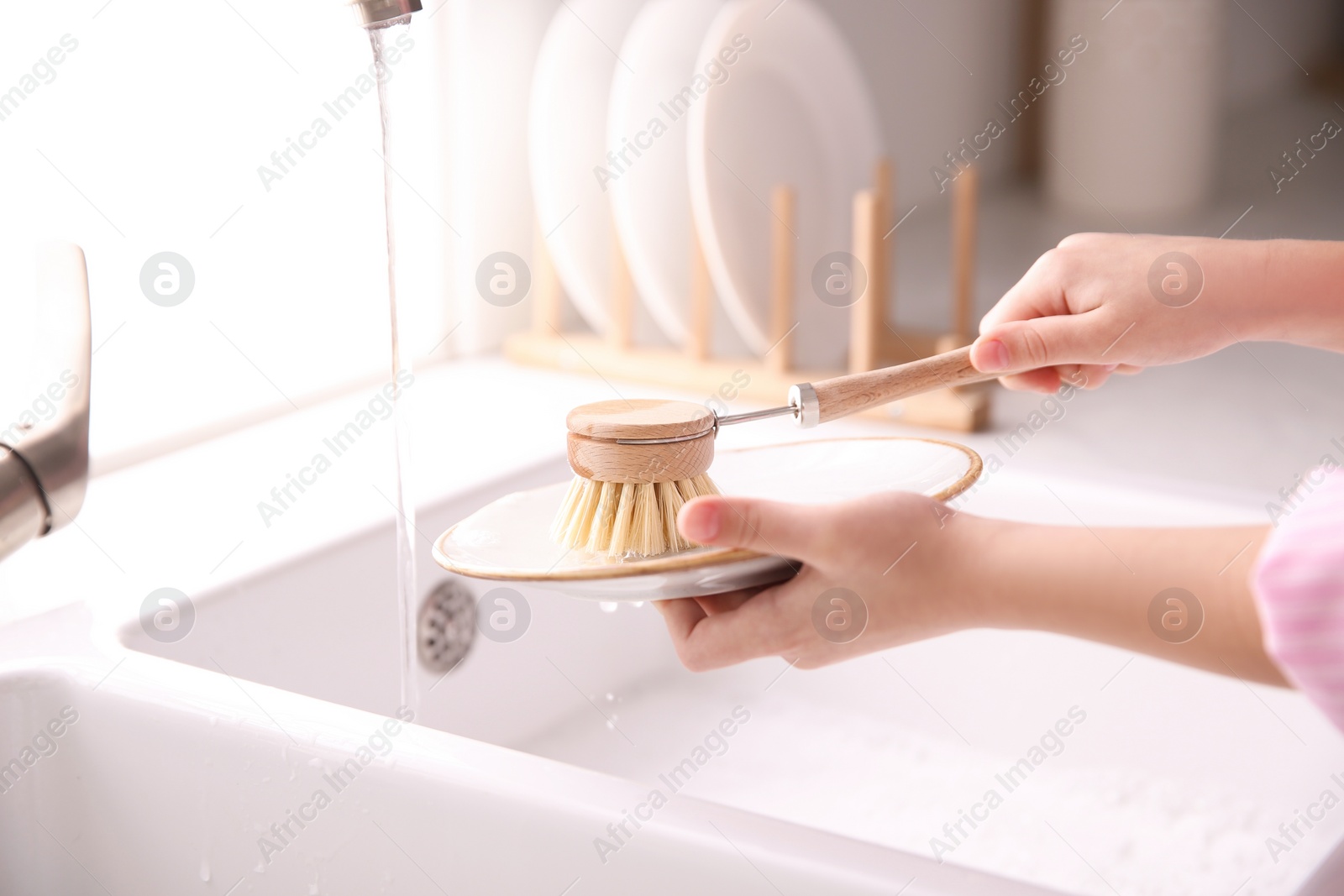 Photo of Little girl washing dishes in kitchen, closeup