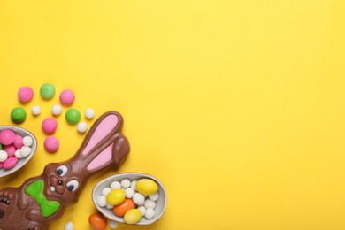 Chocolate Easter bunny, halves of egg and candies on yellow background, flat lay. Space for text