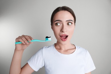 Photo of Surprised woman holding brush with charcoal toothpaste on grey background