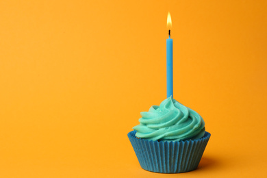 Photo of Delicious birthday cupcake with turquoise cream and burning candle on yellow background. Space for text