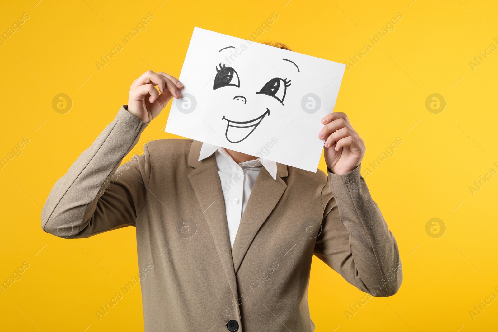 Photo of Woman hiding behind sheet of paper with happy face on yellow background