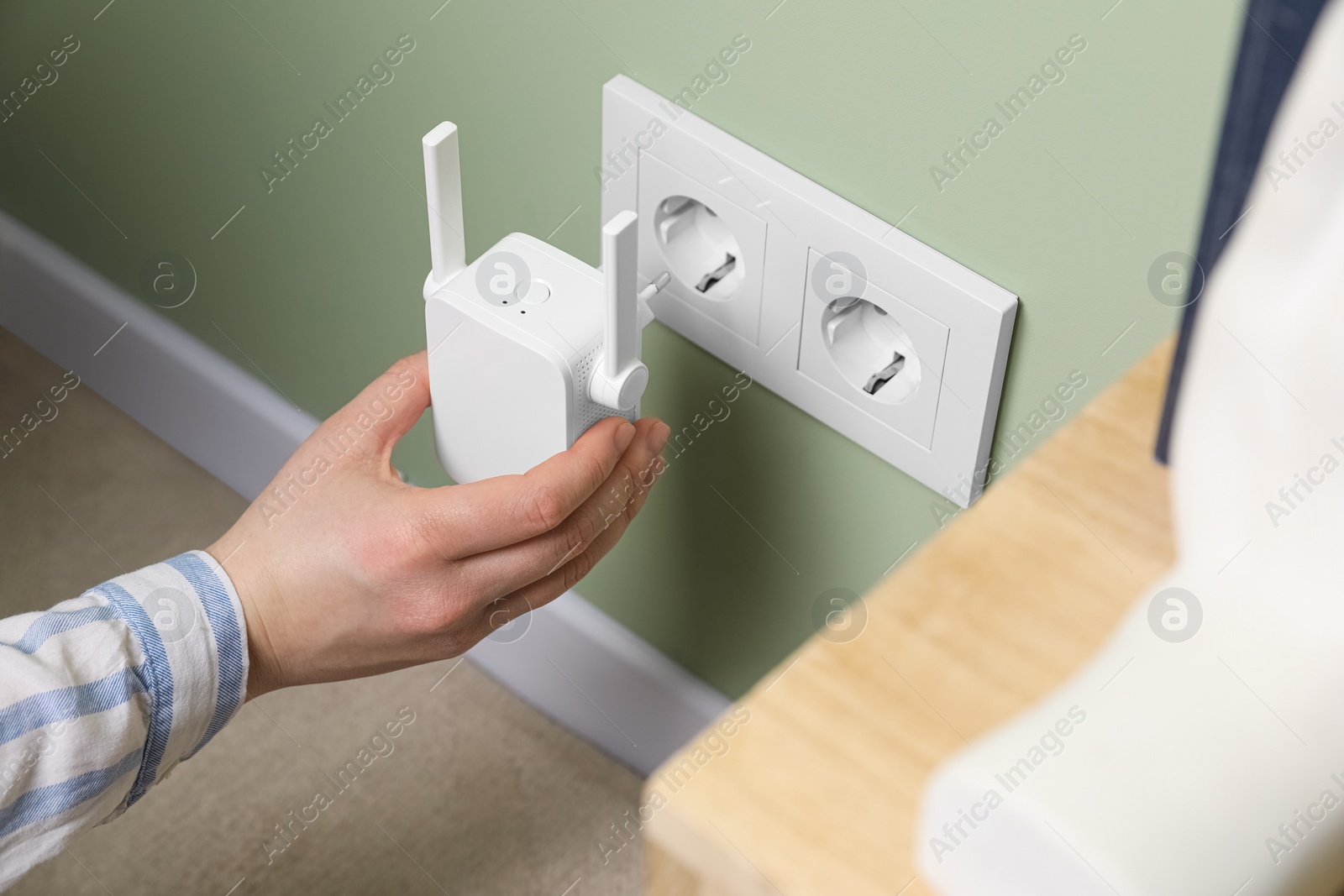 Photo of Woman inserting wireless Wi-Fi repeater into power socket indoors, closeup