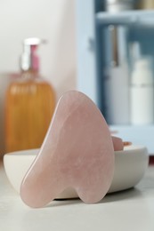 Photo of Rose quartz gua sha tool on white table, closeup