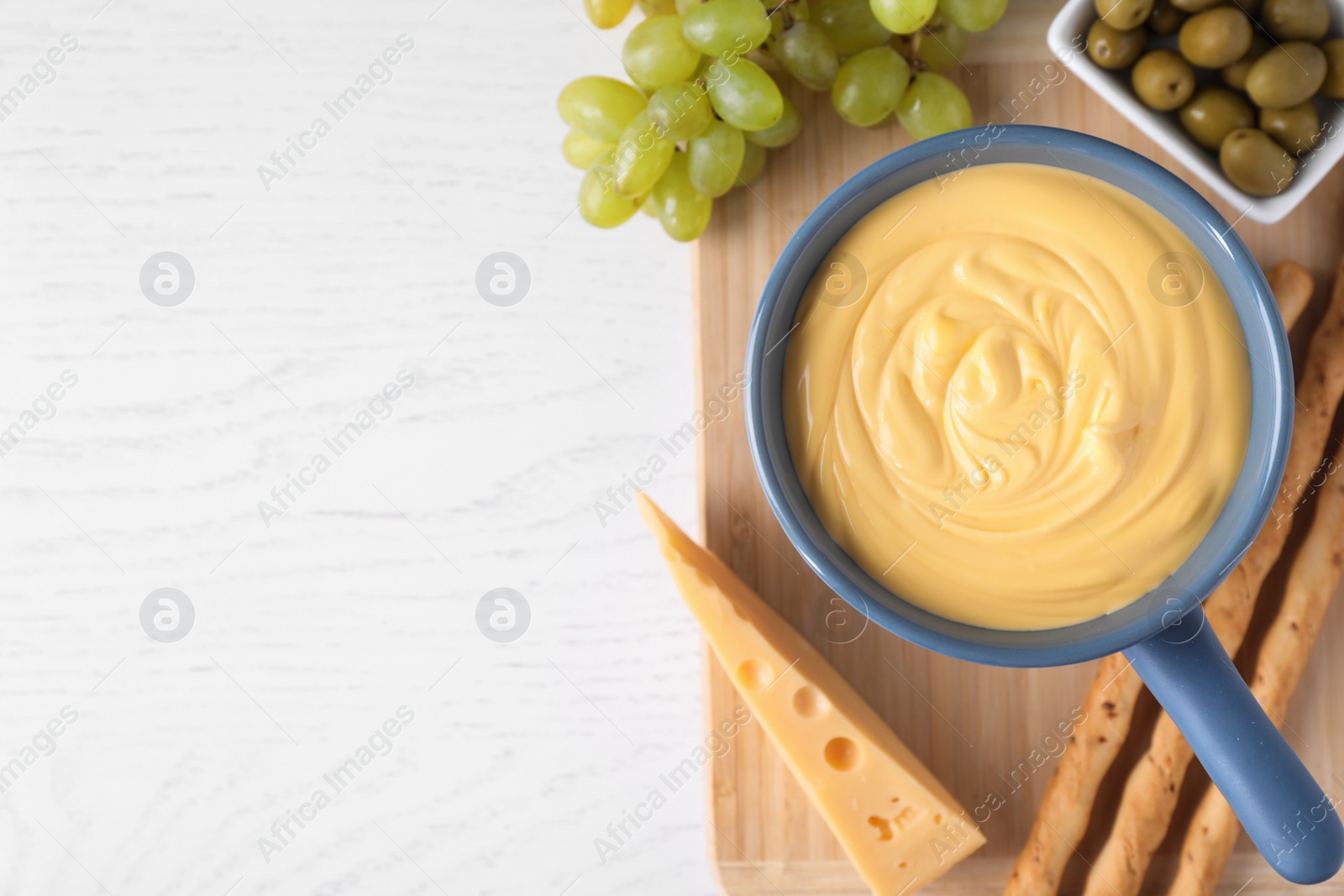 Photo of Flat lay composition with pot of cheese fondue and products on white wooden table, space for text