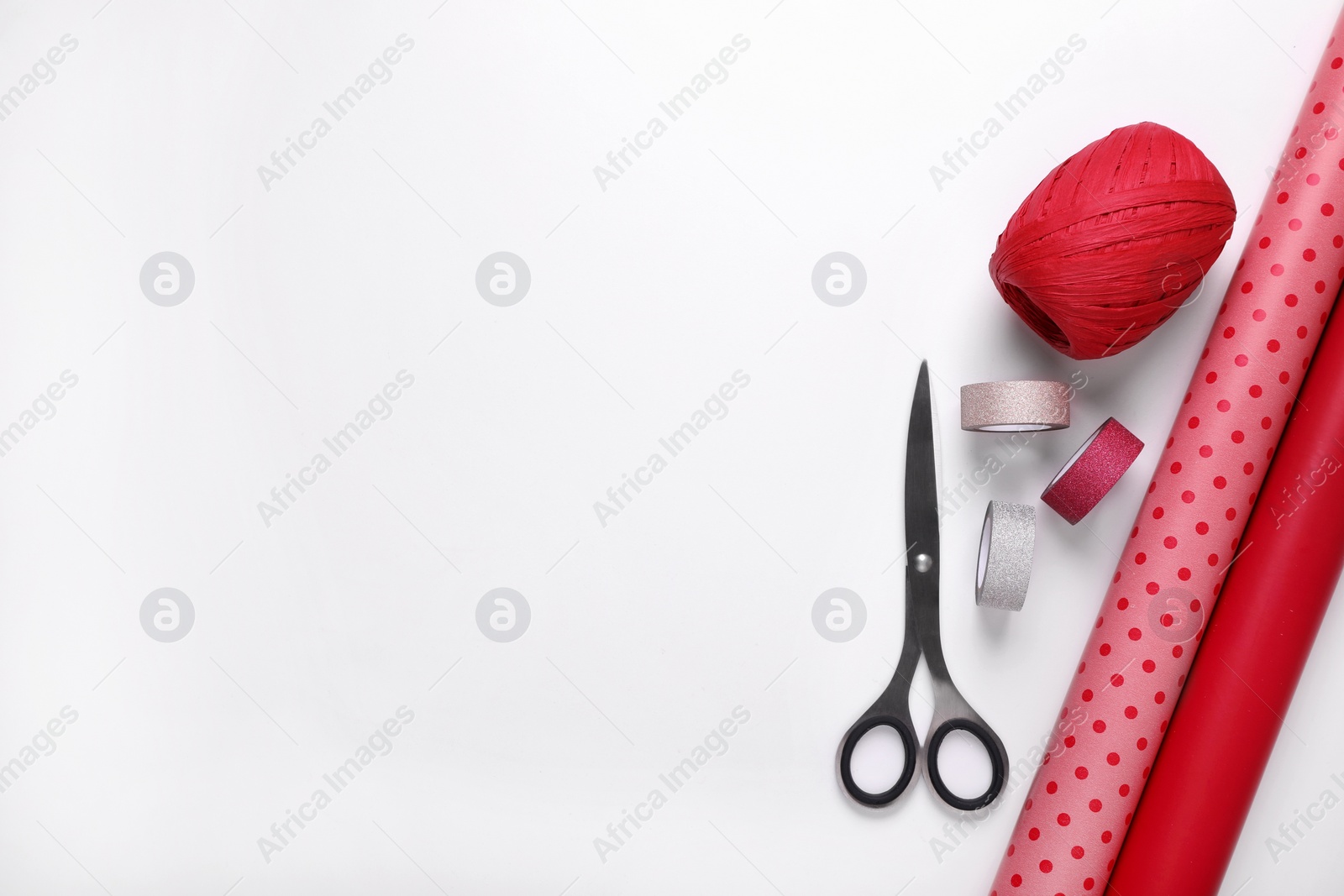 Photo of Rolls of colorful wrapping papers, scissors and ribbons on white background, flat lay. Space for text