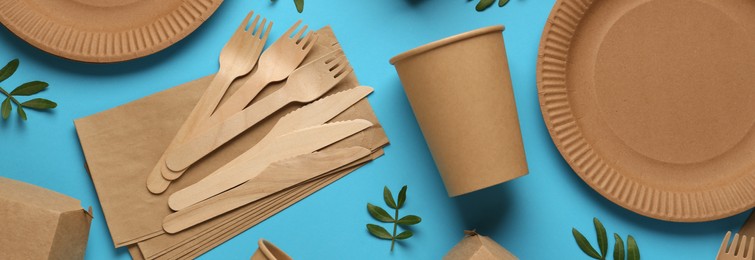 Image of Paper and wooden tableware with green twigs on turquoise background, flat lay. Banner design