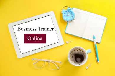 Image of Modern tablet with text BUSINESS TRAINER ONLINE on yellow background, flat lay