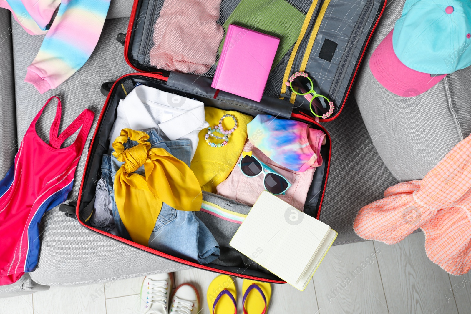 Photo of Open suitcase with stylish clothes and accessories on grey sofa, top view. Summer vacation