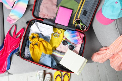 Photo of Open suitcase with stylish clothes and accessories on grey sofa, top view. Summer vacation
