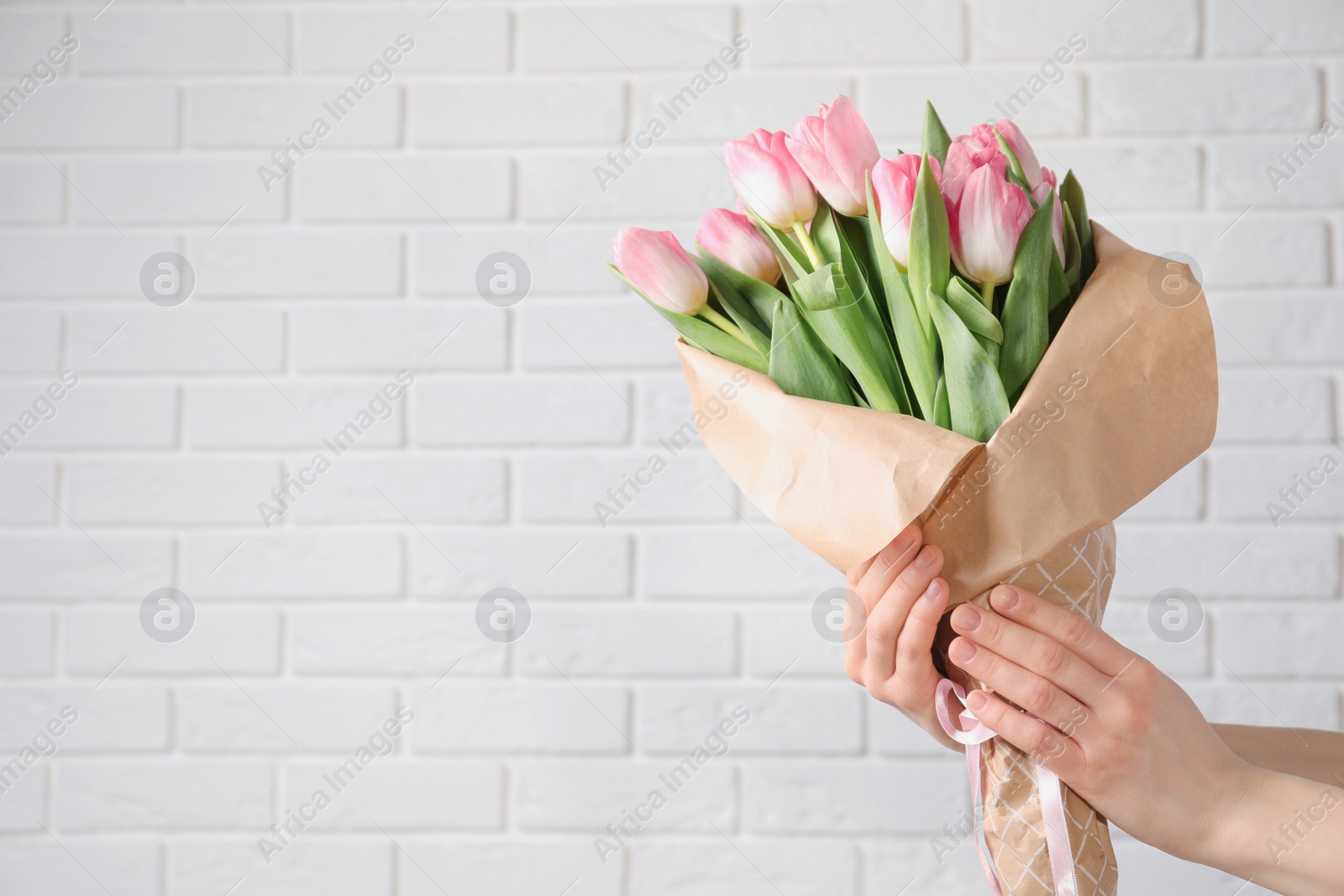 Photo of Girl holding bouquet of beautiful spring tulips near brick wall, closeup with space for text. International Women's Day