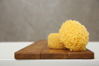Photo of Wooden bath tray with sponges on tub, closeup
