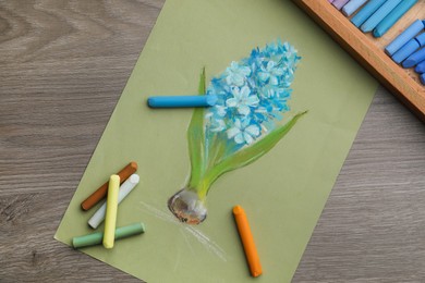 Photo of Beautiful drawing of blooming hyacinth and pastels on wooden table, top view