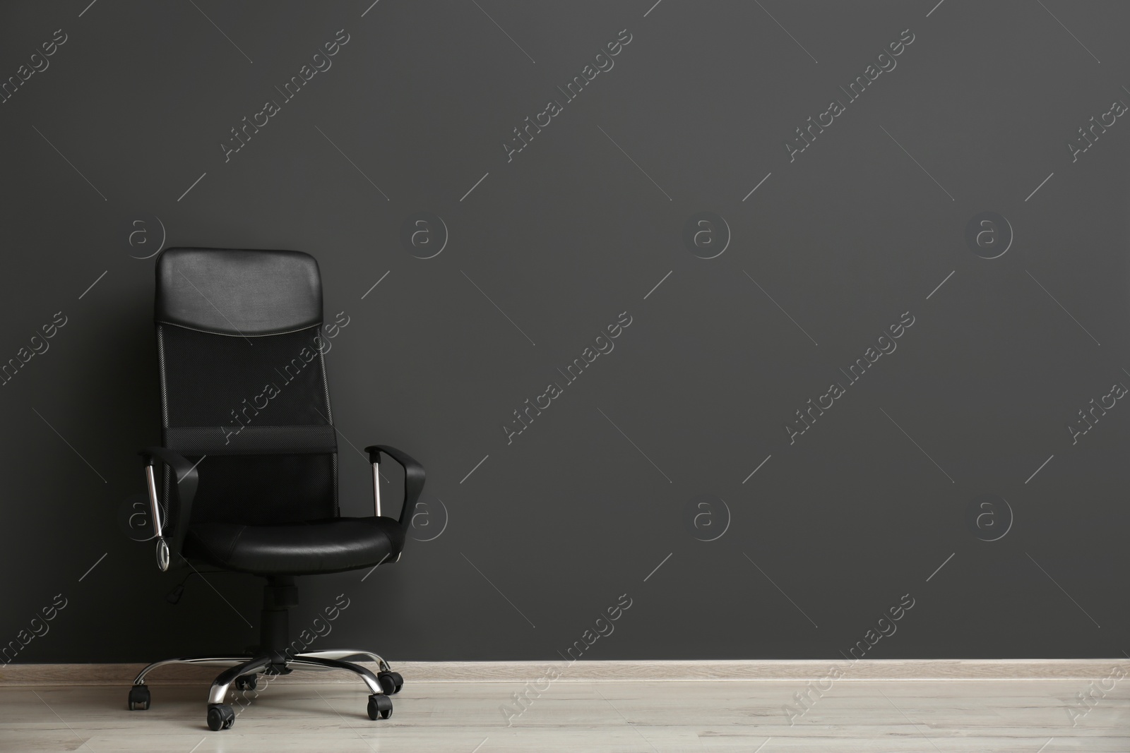 Photo of Comfortable office chair near black wall indoors. Space for text