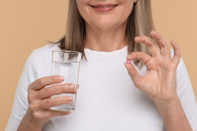 Photo of Senior woman with glass of water and pill on beige background, closeup