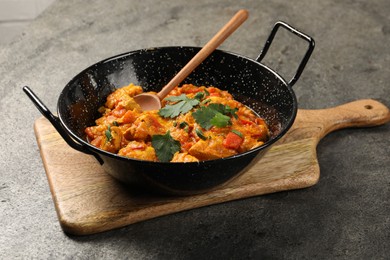 Photo of Delicious chicken curry in frying pan and spoon on grey table