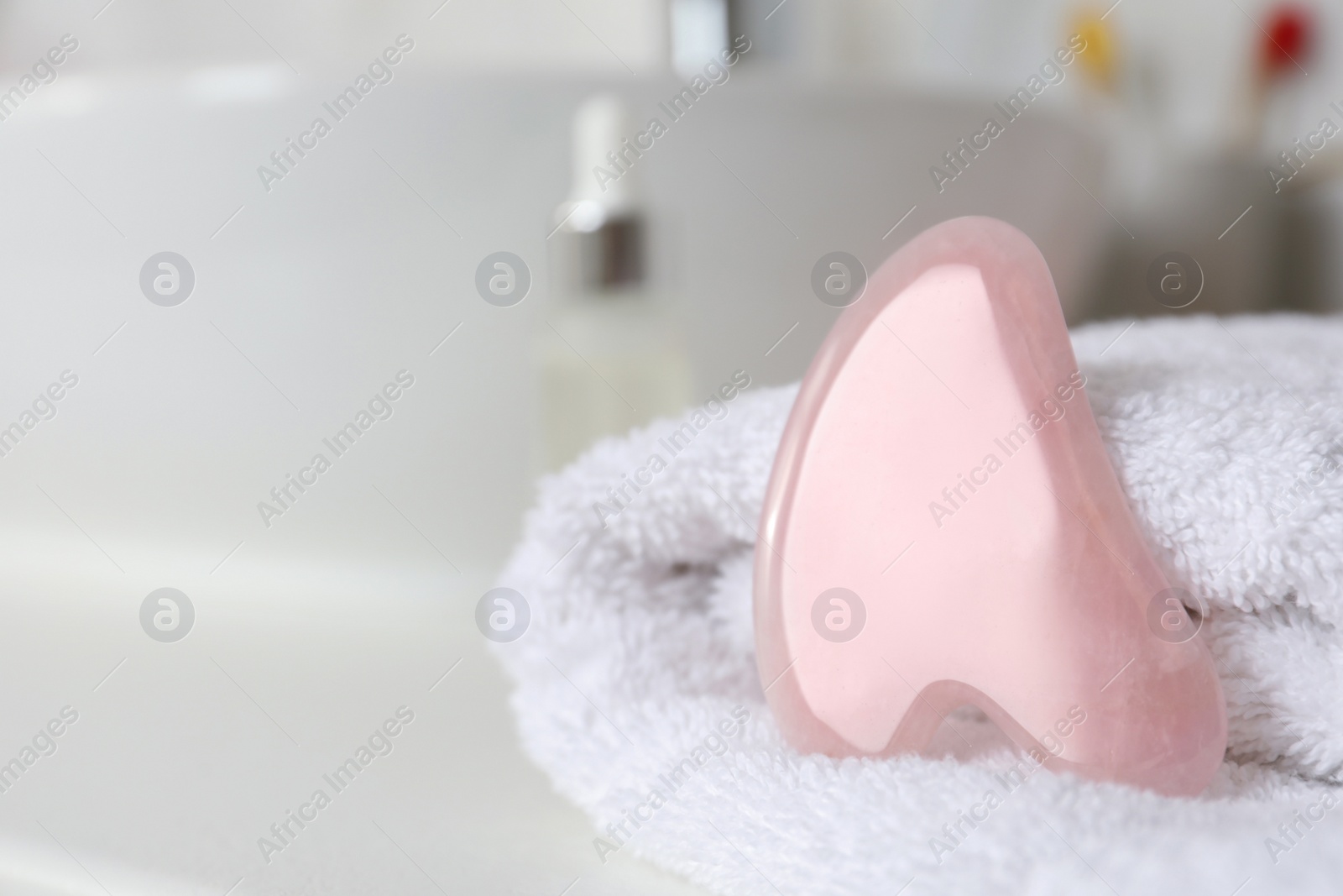 Photo of Rose quartz gua sha tool with soft towel on white table, closeup. Space for text