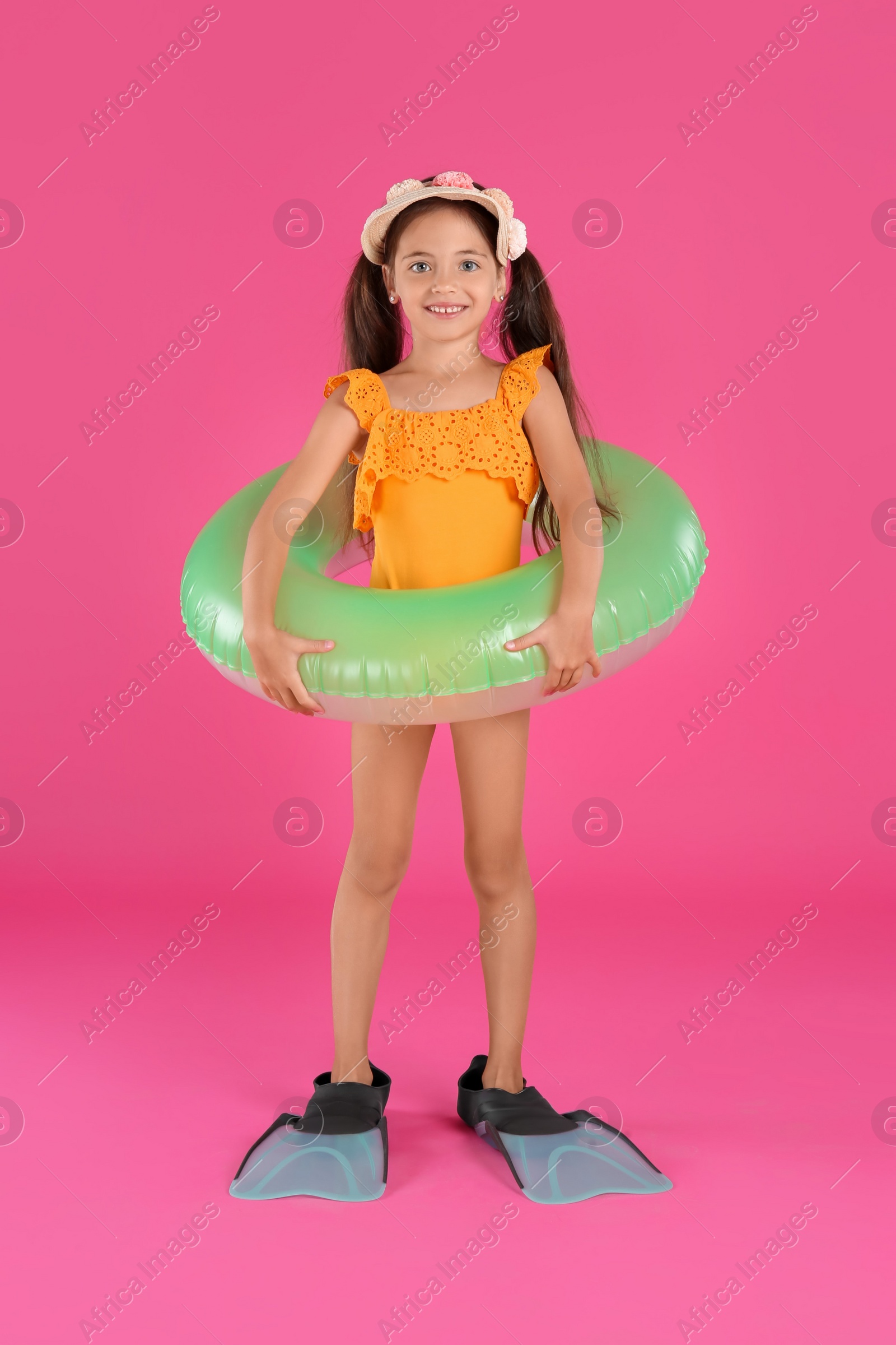 Photo of Cute little child in beachwear with bright inflatable ring on pink background