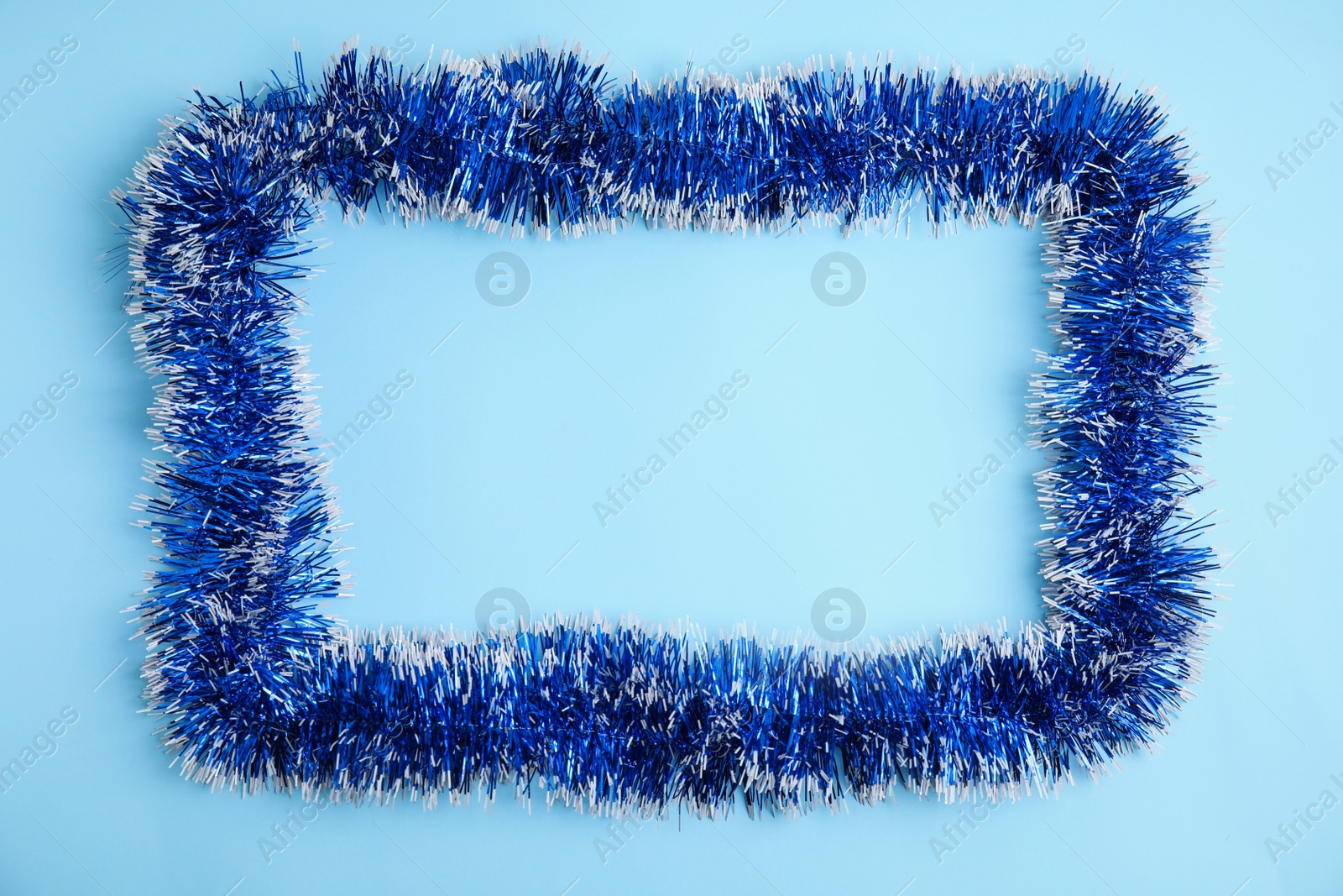 Photo of Frame of bright tinsel on light blue background, top view. Space for text