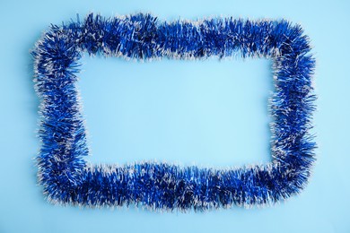 Frame of bright tinsel on light blue background, top view. Space for text