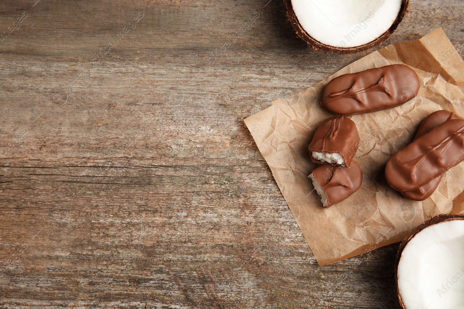 Photo of Delicious milk chocolate candy bars with coconut filling on wooden table, flat lay. Space for text