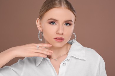 Photo of Beautiful young woman with elegant jewelry on light brown background