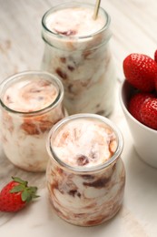 Photo of Tasty yoghurt with jam and strawberries on white marble board, closeup