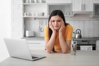 Photo of Young woman suffering from headache in kitchen