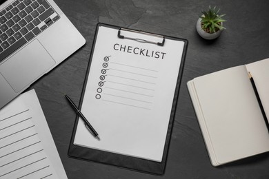Photo of Clipboard with checklist, pen and laptop on black table, flat lay