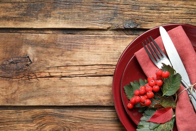 Festive table setting with autumn leaves and ashberries on wooden background, top view. Space for text