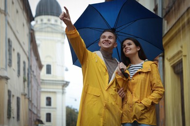 Lovely young couple with umbrella walking under rain on city street