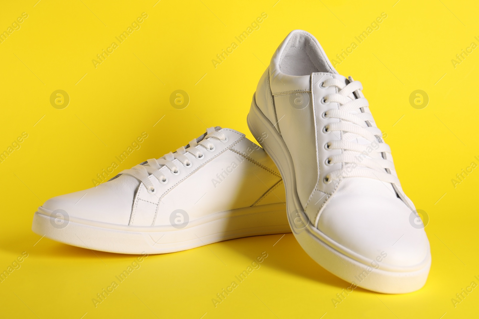 Photo of Pair of stylish white sneakers on yellow background