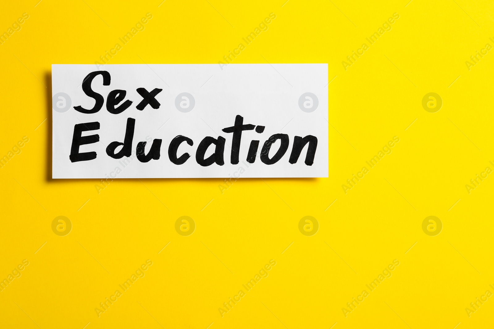 Photo of Piece of paper with phrase "SEX EDUCATION" on yellow background, top view. Space for text