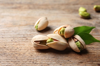 Photo of Organic pistachio nuts on wooden table. Space for text
