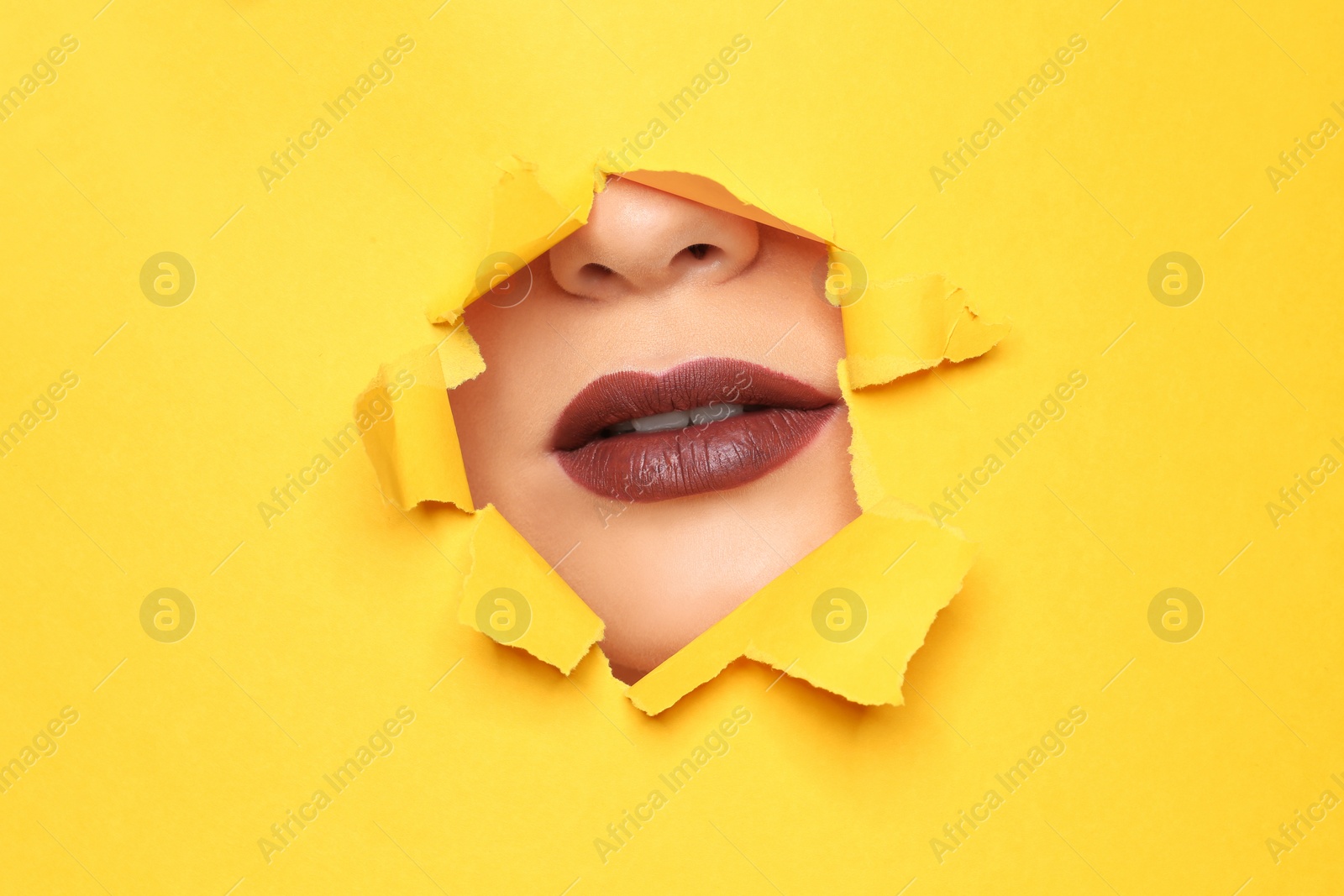 Photo of Lips of beautiful young woman with dark lipstick visible through hole in color paper