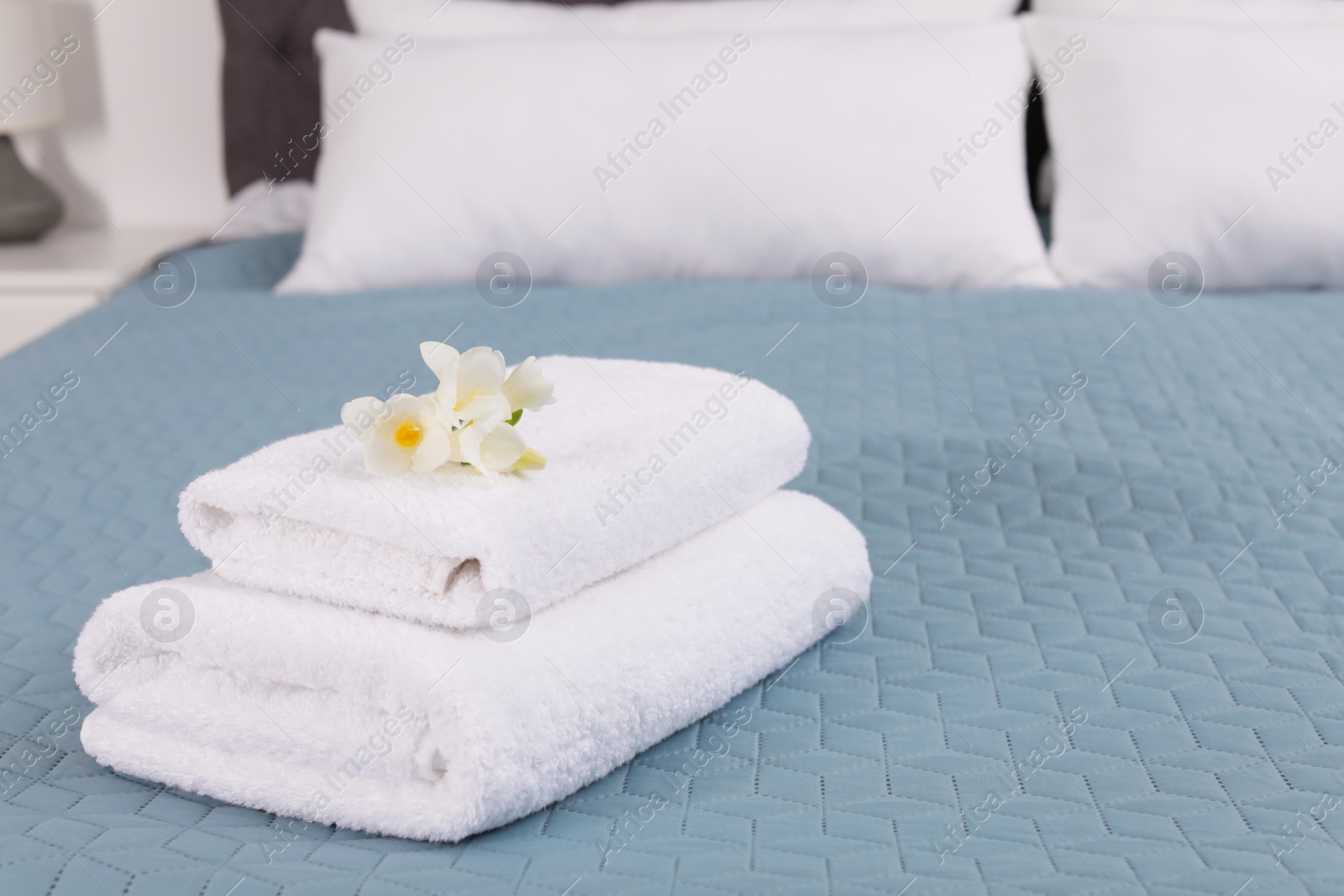 Photo of Stack of fresh towels with flowers on bed in hotel room