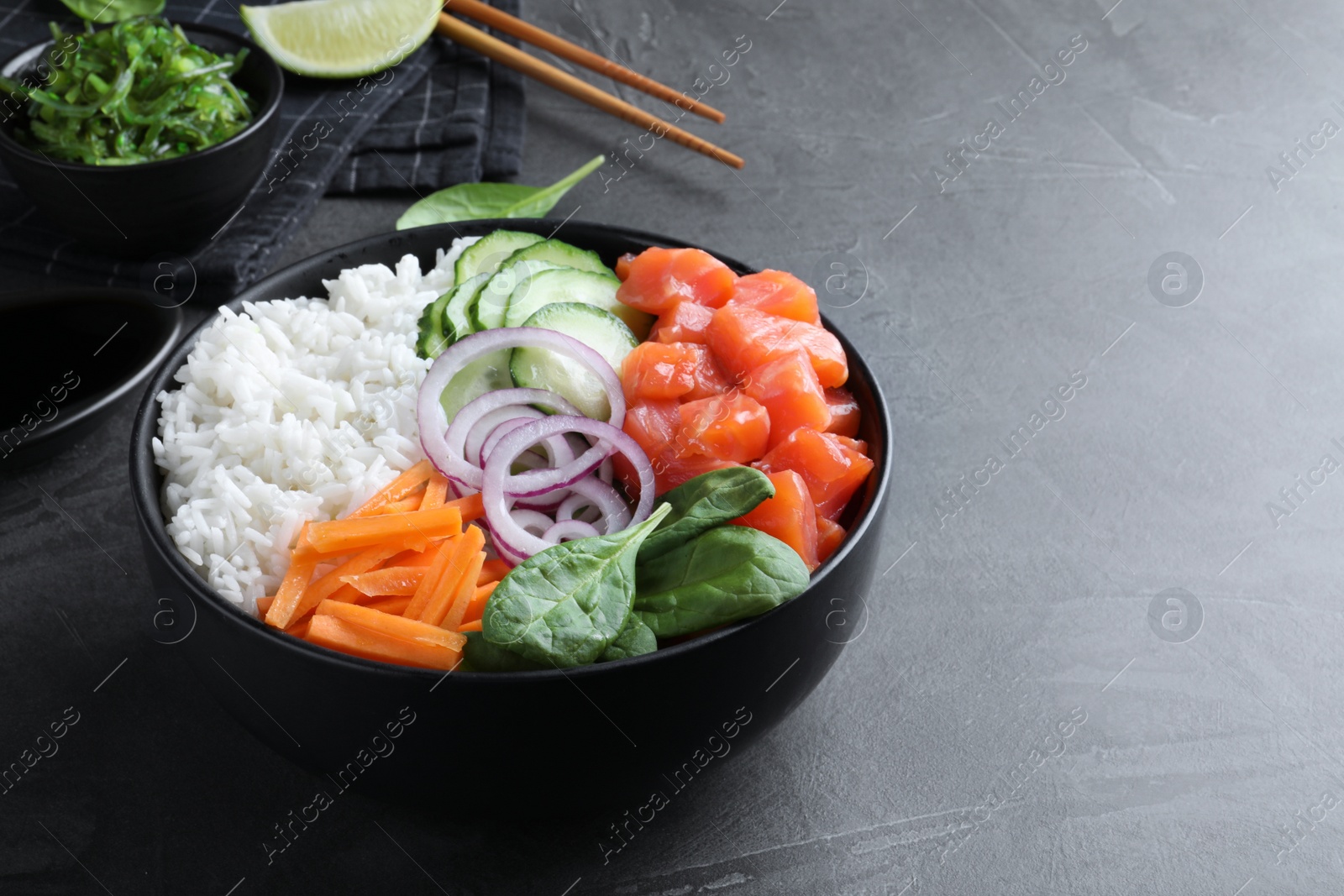 Photo of Delicious poke bowl with salmon and vegetables served on grey table. Space for text