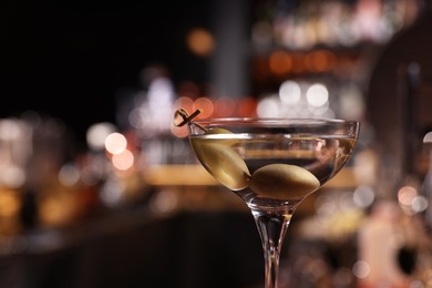 Photo of Martini glass with fresh cocktail and olives against blurred background. Space for text