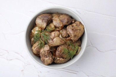 Photo of Tasty fried chicken liver with onion and dill in bowl on white textured table, top view