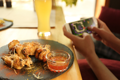 Woman playing game using smartphone at table in cafe, focus on tasty BBQ wings