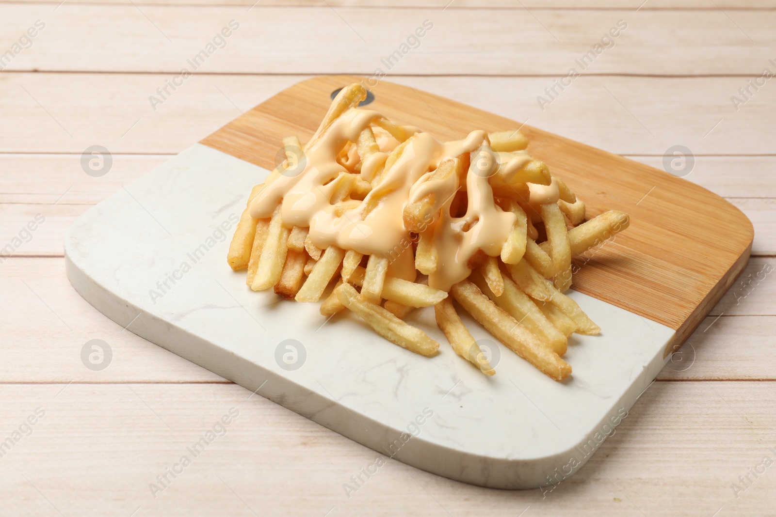 Photo of Delicious french fries with cheese sauce on wooden table