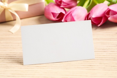 Blank card with space for text, beautiful tulips and gift on wooden table
