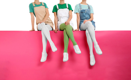 Group of women wearing colorful tights and stylish shoes sitting on color background, closeup