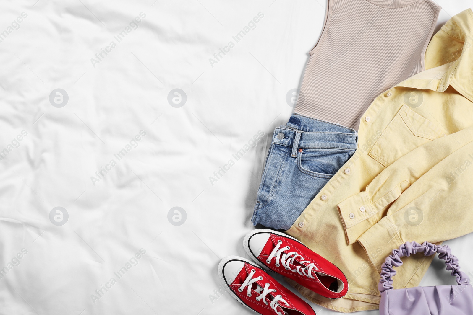 Photo of Pair of stylish red sneakers, clothes and bag on white fabric, flat lay. Space for text