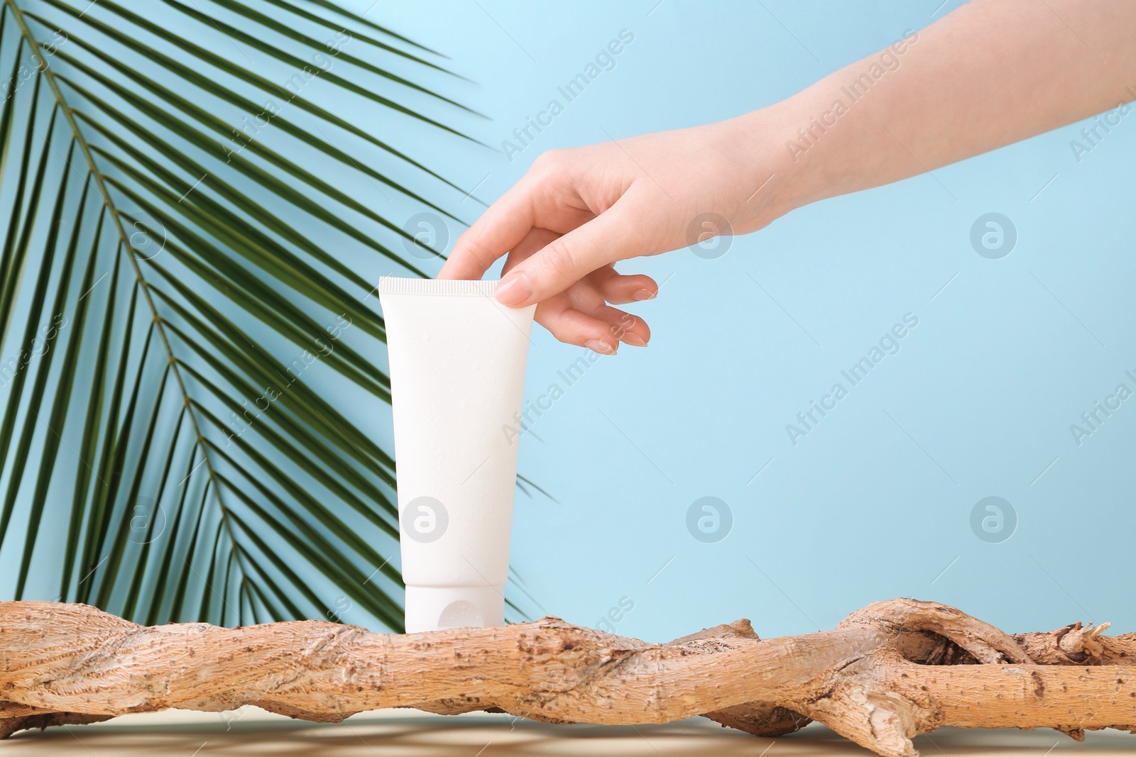 Photo of Woman with tube of cream and plant against light blue background, closeup