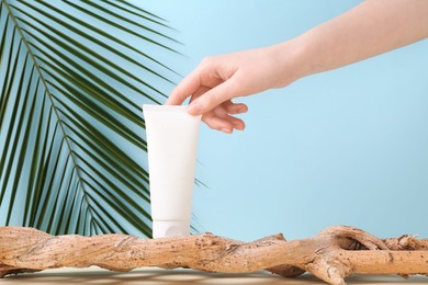 Woman with tube of cream and plant against light blue background, closeup